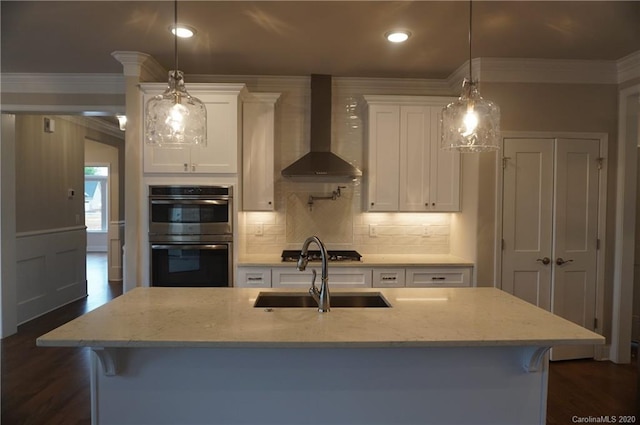 kitchen with hanging light fixtures, appliances with stainless steel finishes, a breakfast bar, white cabinets, and wall chimney exhaust hood