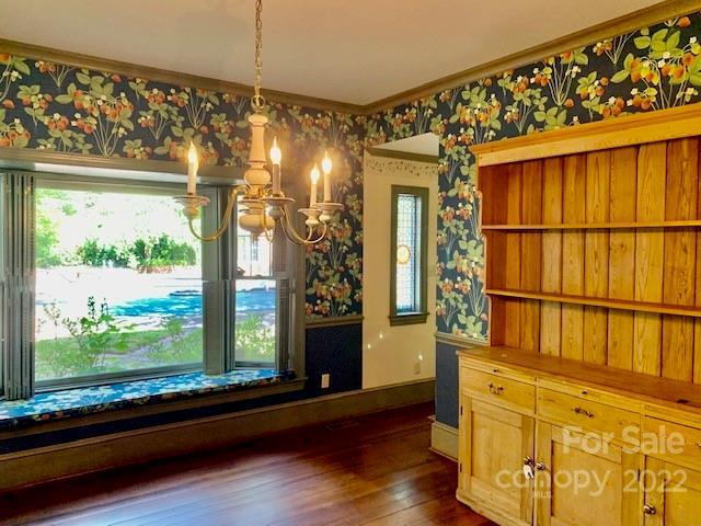 unfurnished dining area featuring a notable chandelier, plenty of natural light, crown molding, and dark wood-type flooring