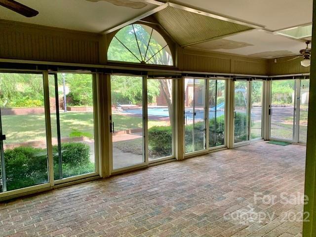 unfurnished sunroom featuring ceiling fan, plenty of natural light, and vaulted ceiling