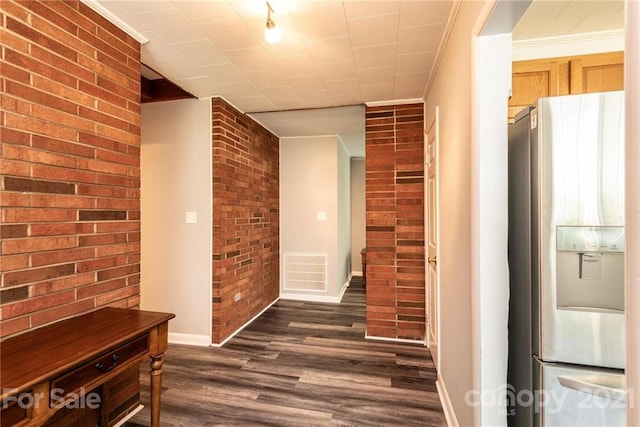 corridor with brick wall, dark wood-type flooring, and ornamental molding