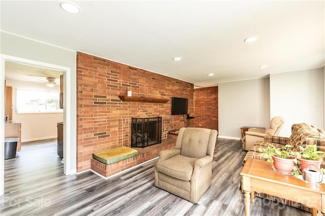 living room with brick wall, dark hardwood / wood-style floors, a brick fireplace, and ceiling fan