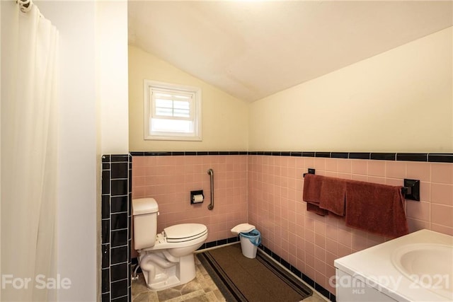 bathroom with toilet, vanity, lofted ceiling, tile walls, and tile floors