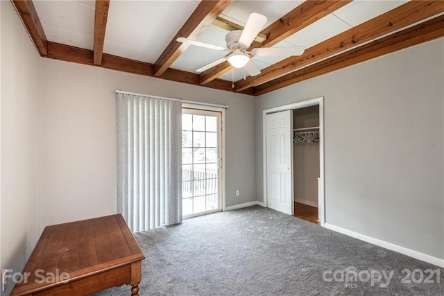 unfurnished bedroom featuring ceiling fan, a closet, dark colored carpet, and beamed ceiling