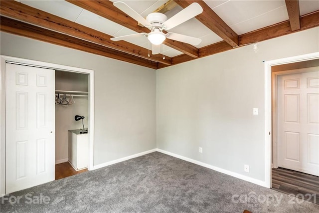 unfurnished bedroom featuring beam ceiling, ceiling fan, dark colored carpet, and a closet