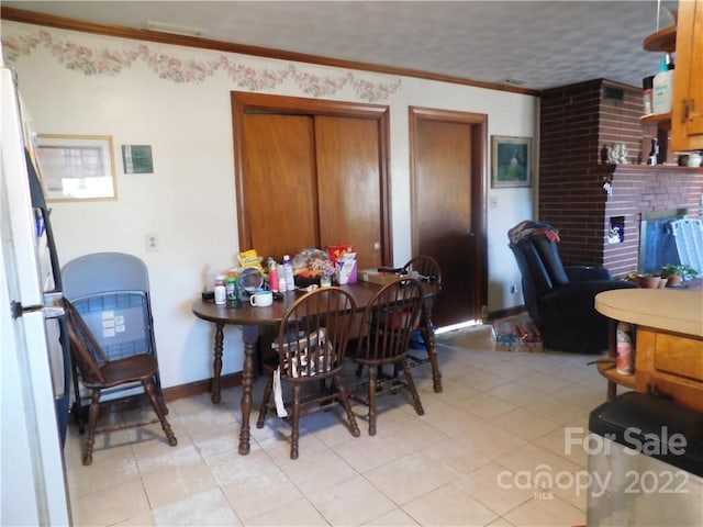 dining space with a brick fireplace, a textured ceiling, ornamental molding, and light tile floors