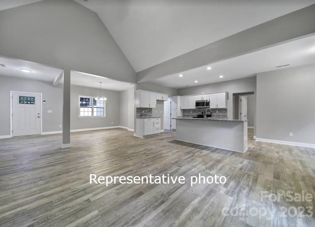 unfurnished living room featuring an inviting chandelier, high vaulted ceiling, and light hardwood / wood-style floors