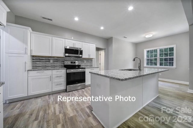 kitchen with light hardwood / wood-style floors, stainless steel appliances, white cabinets, and a center island with sink