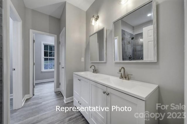 bathroom featuring hardwood / wood-style floors, a tile shower, and dual bowl vanity