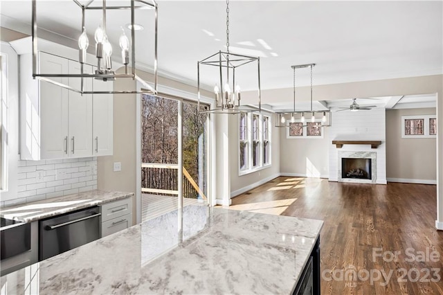 kitchen with light stone countertops, dark wood-type flooring, a large fireplace, ceiling fan with notable chandelier, and white cabinetry