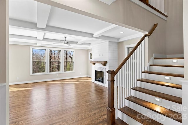 stairway with a high end fireplace, ceiling fan, coffered ceiling, dark wood-type flooring, and beam ceiling