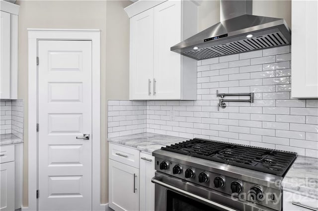 kitchen featuring high end stainless steel range oven, white cabinetry, wall chimney exhaust hood, light stone counters, and tasteful backsplash