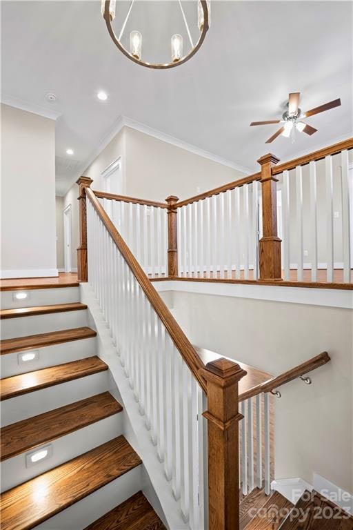 staircase with hardwood / wood-style floors, crown molding, and ceiling fan with notable chandelier