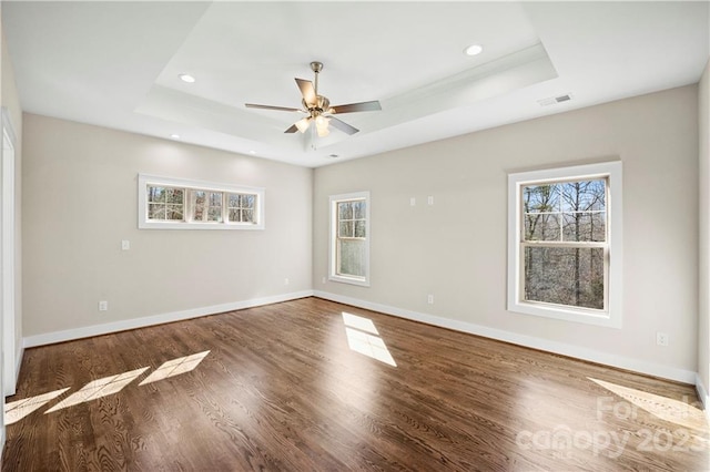 empty room with ceiling fan, dark hardwood / wood-style floors, and a raised ceiling