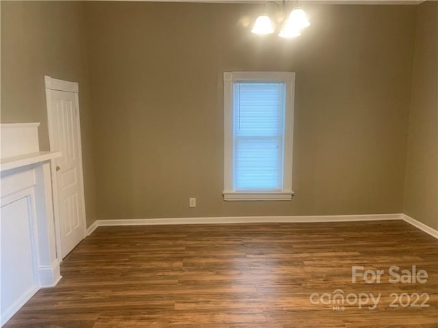 unfurnished living room featuring an inviting chandelier and dark wood-type flooring