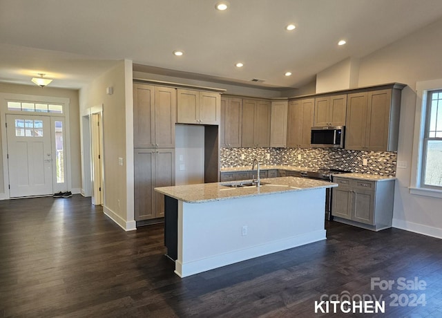 kitchen with a kitchen island with sink, vaulted ceiling, appliances with stainless steel finishes, light stone countertops, and sink