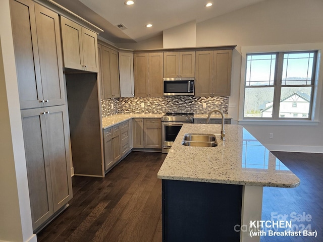 kitchen with sink, vaulted ceiling, light stone countertops, a center island with sink, and appliances with stainless steel finishes