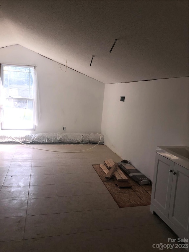 bonus room with dark tile flooring, a textured ceiling, and vaulted ceiling