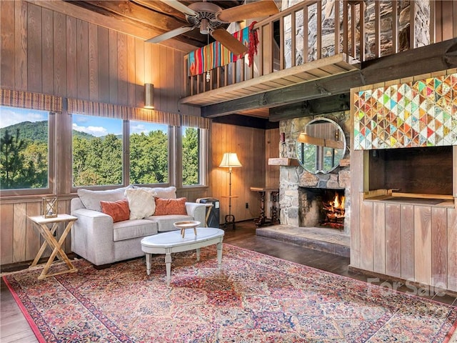 living room featuring dark wood-type flooring, ceiling fan, wooden walls, a fireplace, and a high ceiling