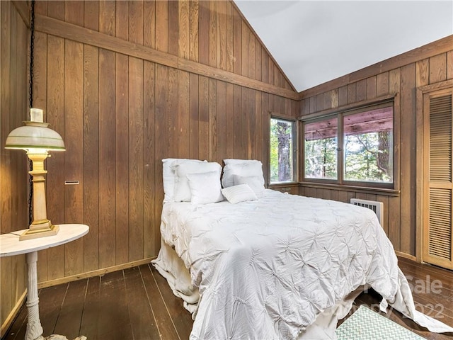 bedroom featuring a wall unit AC, dark hardwood / wood-style flooring, wooden walls, and vaulted ceiling