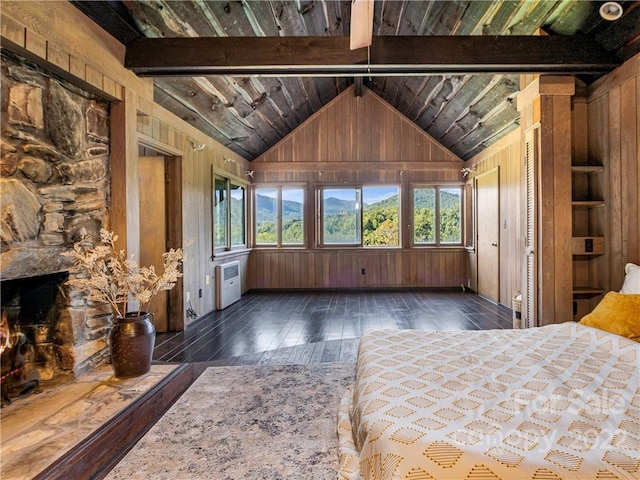 unfurnished bedroom with wooden walls, a stone fireplace, dark wood-type flooring, and lofted ceiling with beams