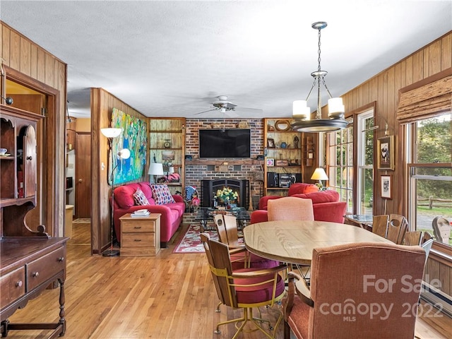 dining room featuring brick wall, light hardwood / wood-style floors, wood walls, and a brick fireplace