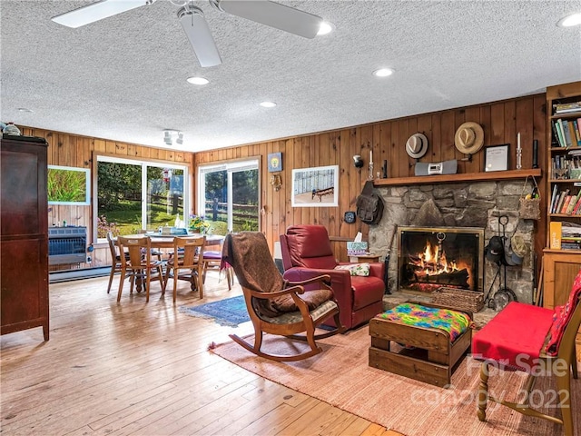 interior space with ceiling fan, a fireplace, wood walls, a textured ceiling, and light hardwood / wood-style flooring