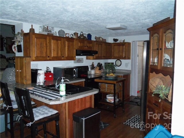 kitchen with a breakfast bar area, a textured ceiling, sink, dark hardwood / wood-style floors, and range hood