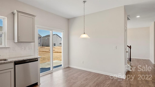 kitchen featuring light stone counters, dishwasher, backsplash, decorative light fixtures, and light wood-type flooring