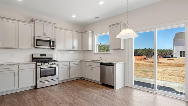 kitchen featuring appliances with stainless steel finishes, backsplash, hardwood / wood-style floors, and pendant lighting