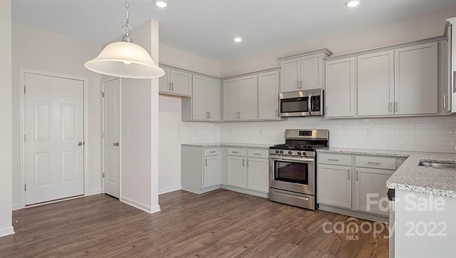 kitchen with appliances with stainless steel finishes, backsplash, decorative light fixtures, dark hardwood / wood-style flooring, and light stone countertops