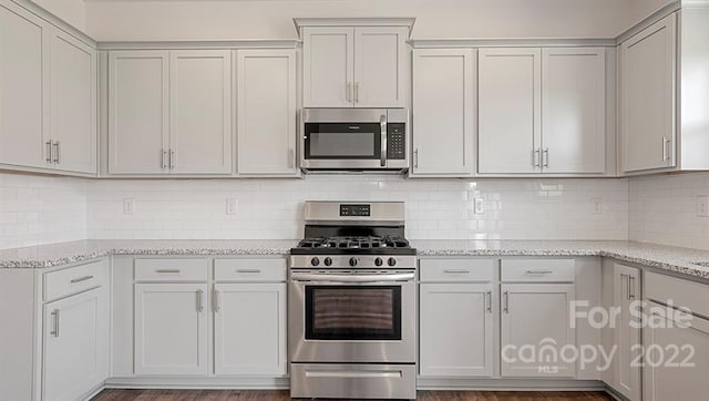 kitchen featuring stainless steel appliances, white cabinets, dark wood-type flooring, and light stone counters