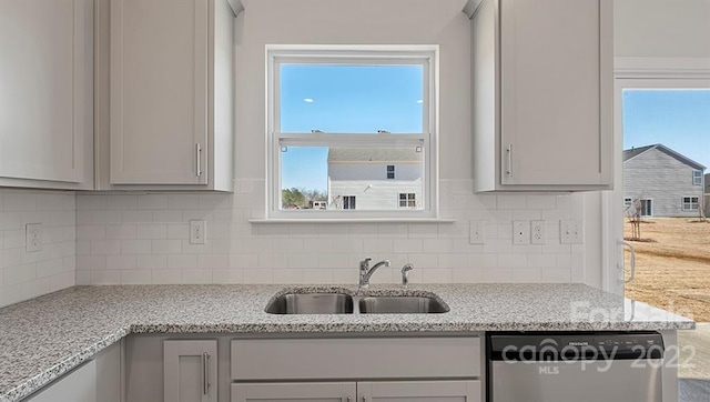 kitchen with backsplash, sink, light stone countertops, gray cabinets, and dishwashing machine