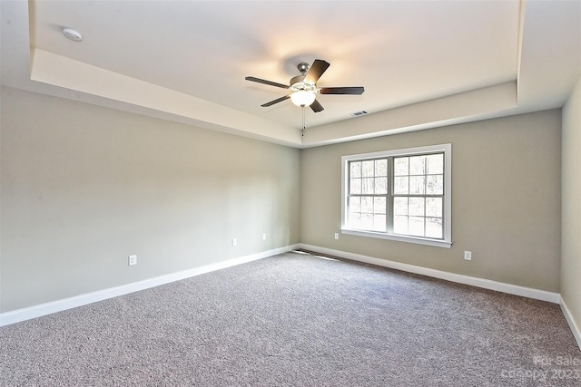 spare room with ceiling fan, a tray ceiling, and carpet