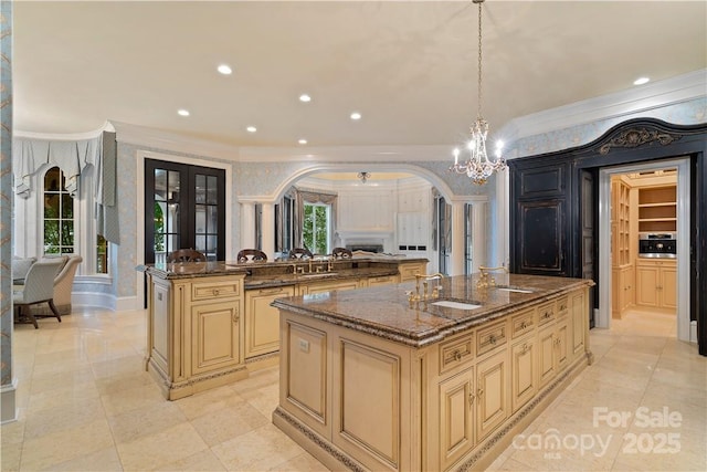 kitchen featuring hanging light fixtures, an island with sink, ornamental molding, and dark stone counters