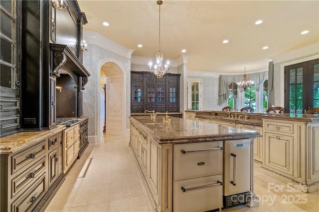 kitchen featuring pendant lighting, crown molding, a large island with sink, dark stone counters, and a chandelier