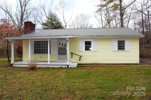 view of front of property featuring a chimney, metal roof, and a front yard