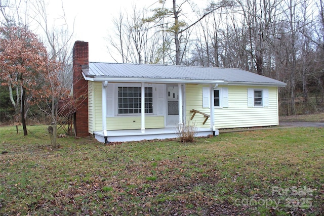 view of front facade with metal roof, a porch, a chimney, and a front yard