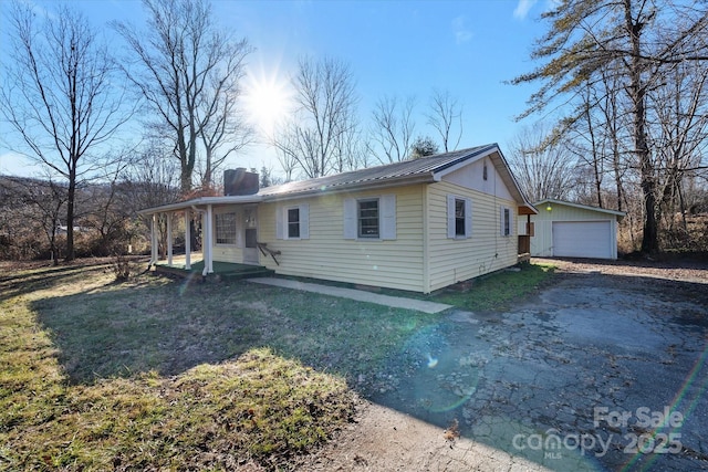 view of front of property featuring a garage, a chimney, aphalt driveway, metal roof, and an outbuilding