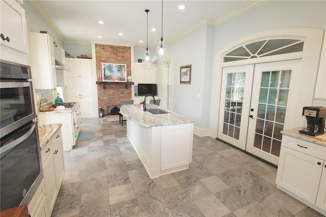 kitchen featuring decorative light fixtures, stainless steel double oven, an island with sink, white cabinets, and french doors