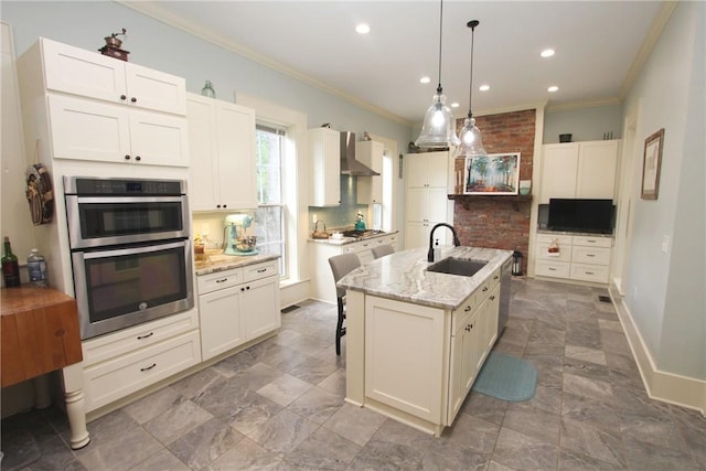 kitchen with an island with sink, decorative light fixtures, wall chimney exhaust hood, appliances with stainless steel finishes, and sink