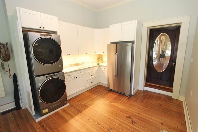 laundry area featuring cabinets, stacked washer and clothes dryer, light hardwood / wood-style floors, and crown molding