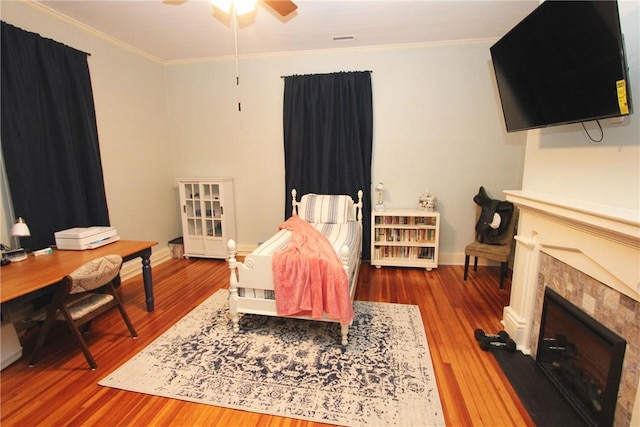 bedroom with dark hardwood / wood-style flooring, a tiled fireplace, ceiling fan, and crown molding