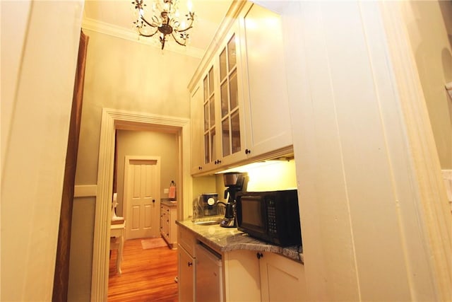 kitchen with a chandelier, dark stone counters, ornamental molding, wood-type flooring, and sink