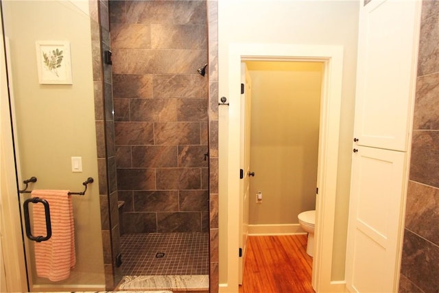 bathroom with toilet, a tile shower, and hardwood / wood-style floors