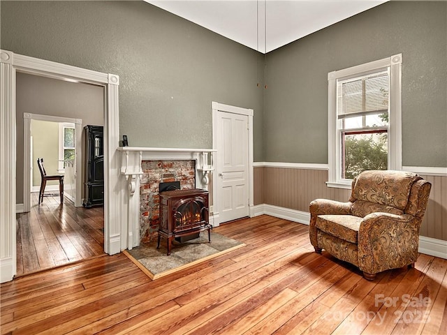 living area with wood-type flooring, a wood stove, baseboards, and wainscoting
