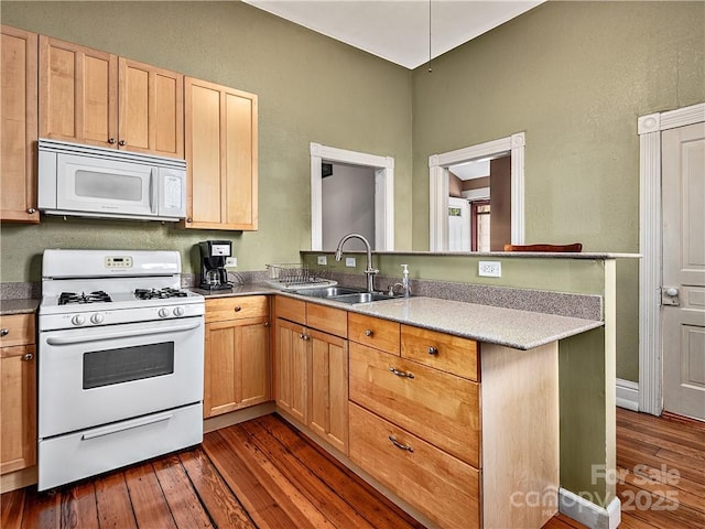 kitchen with dark wood-style floors, light brown cabinets, a sink, white appliances, and a peninsula