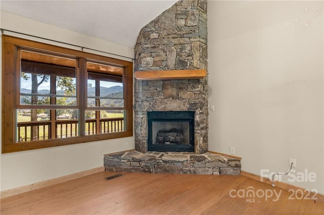 unfurnished living room with lofted ceiling, a stone fireplace, and light hardwood / wood-style flooring