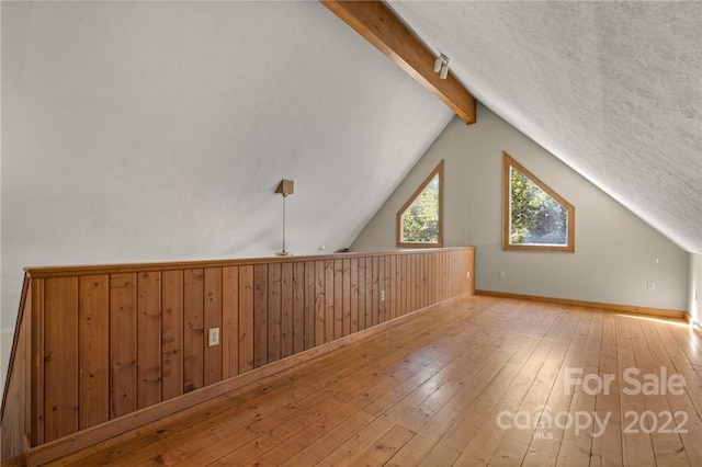 additional living space featuring vaulted ceiling with beams, light hardwood / wood-style floors, and a textured ceiling