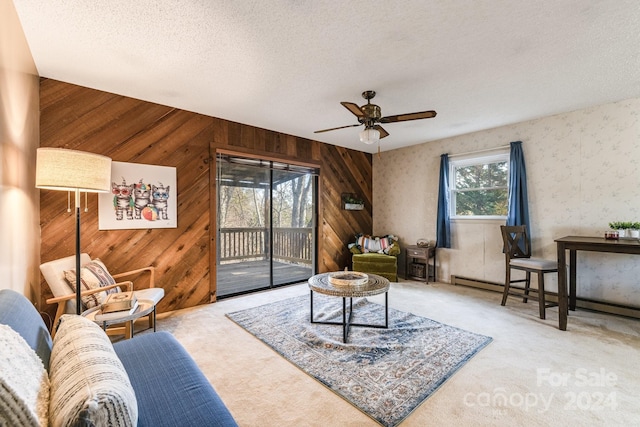 living area featuring carpet flooring, wood walls, ceiling fan, and a textured ceiling