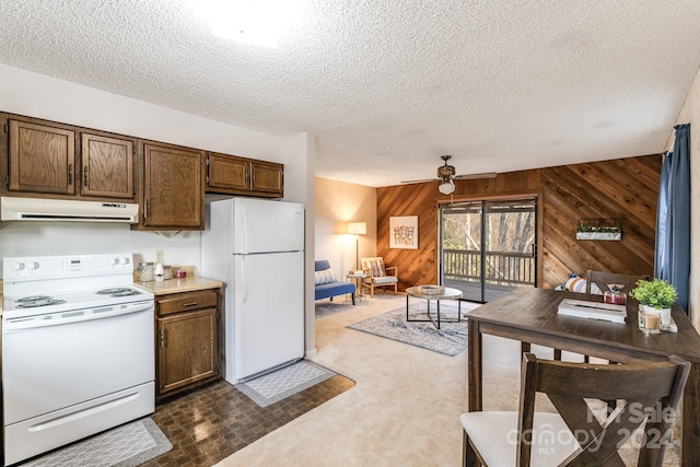 kitchen with white appliances, a textured ceiling, wood walls, ceiling fan, and dark colored carpet